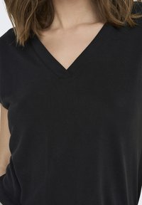 T-shirt noir à col en V fabriqué en tissu lisse. Manches courtes, silhouette ajustée et détail de couture subtil au niveau de l'encolure.