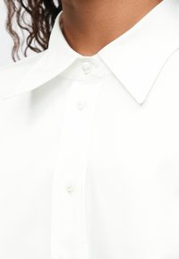 White cotton shirt with a classic collar, featuring a button-down front and smooth texture. Lightweight fabric with subtle sheen.
