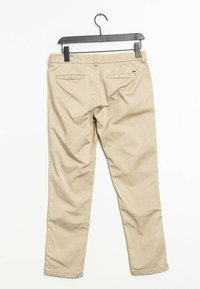 Beige byxor upphängda på en svart galge. Har ett slätt tyg, rak benmodell och två bakfickor med knappdetaljer.