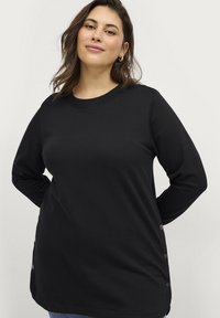 Camisa de manga larga negra hecha de una tela suave, con un escote redondo y detalles de botones en el costado para mayor estilo.