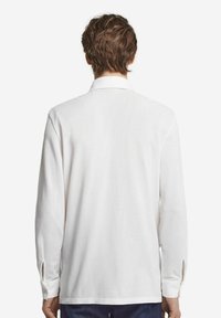 Camicia bianca a maniche lunghe con collo classico, fessure laterali e polsini con bottone, realizzata in un tessuto leggero e testurizzato.