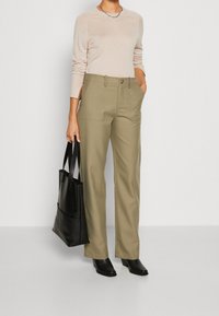 Helles rosa Langarmshirt, olivgrüne hochgeschnittene Hose mit vorderen Taschen, schwarze Leder-Tote-Tasche und schwarze Absatz-Stiefeletten.