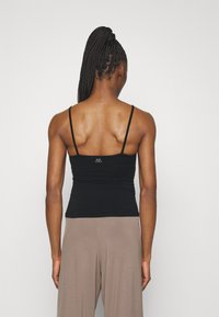 Black fitted tank top with thin straps, made of smooth fabric. Features a small logo on the back. Paired with light brown wide-leg pants.