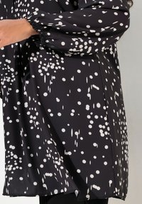 Czarna bluzka w biały wzór w kropki, z długimi rękawami ze ściągaczami i luźnym krojem. Gładki, lekki materiał.