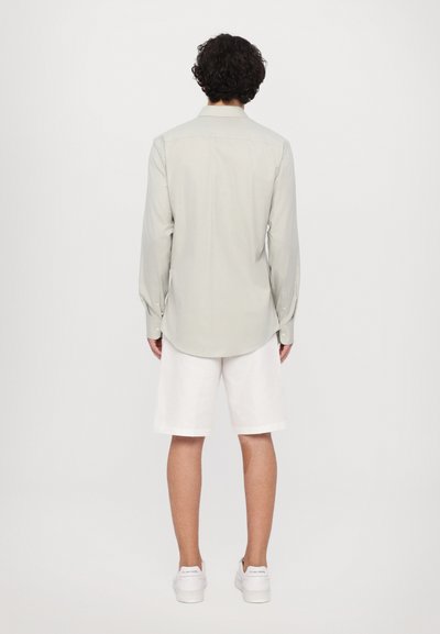 Cămașă gri deschis, cu mânecă lungă, asociată cu pantaloni scurți albi, purtată cu teniși albi. Design simplu, fără modele vizibile.