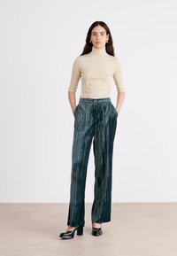 Topsi turtleneck vaaleanbeige yhdistetty tummanvihreisiin, laskostettuihin leveälahkeisiin housuihin. Kankaan pinnassa on hienovarainen kiilto ja pystysuora raidoitus.