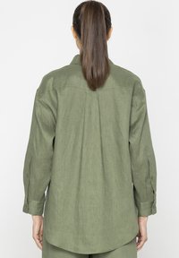 Zielona, długosleeve koszula wykonana z teksturowanej, lekkiej tkaniny. Posiada zapinane mankiety oraz zaokrąglony dół, z detalem na plecach.
