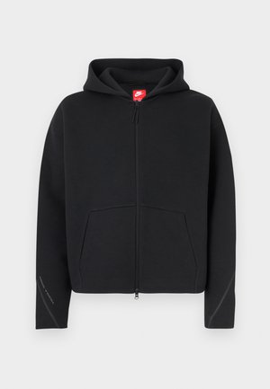 Sudadera negra con cremallera, bolsillo frontal, tela texturizada, capucha con cordones y logo rojo de Nike en la etiqueta del cuello. Detalles de costuras en las mangas.