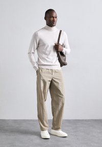 Light beige turtleneck sweater, relaxed cream trousers, and white sneakers. Brown leather bag with shoulder strap. Minimalist design.