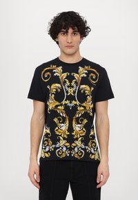 T-shirt preta de algodão com padrões florais barrocamente intrincados em dourado e branco na frente. Mangas curtas, design de gola redonda.