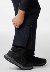 Zwarte waterdichte wandelpants met ritssluitingen aan de zijkant, gecombineerd met zwarte hoge wandelschoenen met gestructureerde oppervlakken en grijze accenten.