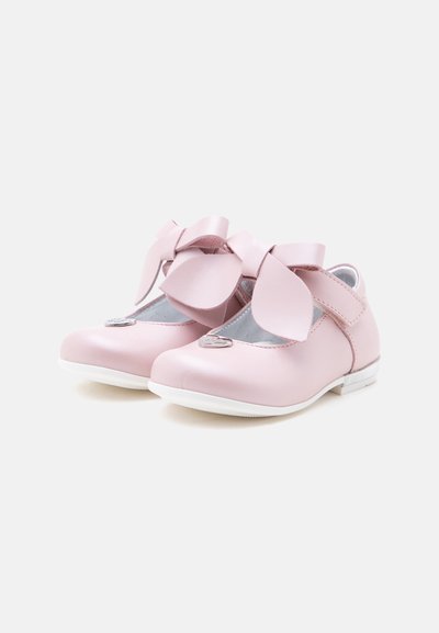 Paire de chaussures roses pour tout-petits avec de grands nœuds sur le dessus et des semelles blanches sur un fond clair uni.