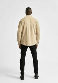Beige långärmad skjorta med en något rundad nederkant, ryggsömn och knappmanschetter, tillsammans med svarta slim-fit jeans och svarta stövlar.