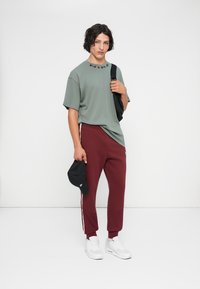 Siva majica s tekstom "NIKE", bordo uske trenirke z belimi stranicami, črna kapa in bele superge. Preprost, športen videz.