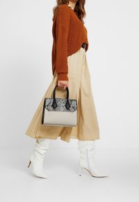 Strukturväska i beige med ett texturerat grått ormskinnslock och svarta detaljer. Har korta svarta handtag och en stilren design.