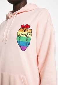 Sudoñ rosa con un colorido diseño de corazón bordado en rayas arcoíris y una corona roja en la parte superior. Material de algodón, corte relajado.