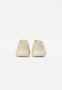 Beige színű sneaker, sima bőrből készült felsőrésszel, párnázott talppal és kerek orral. Két színű díszítéssel rendelkezik a sarkán és diszkrét logóval.