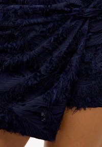 Robe bleu marine texturée avec des détails superposés et effilochés, créant un motif de vagues. Le tissu semble doux avec un léger éclat.