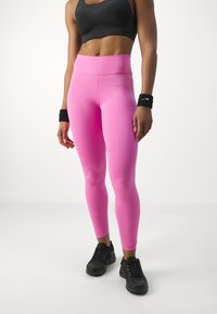 Höga, figurnära leggings i klarröd färg, tillsammans med svarta sportskor och handledsband. Slät textur, elastiskt material.