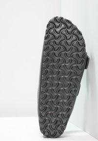 Semelle de chaussure noire avec un motif texturé en vagues, fabriquée en caoutchouc durable. Vue de côté montrant un dessus lisse et un léger talon.