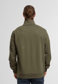 Pullover in pile verde oliva con colletto alto, polsini e orlo a coste. Texture morbida, vestibilità casual, design semplice e senza loghi visibili.