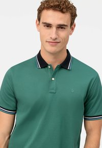 Polo verde con colletto nero, patta con tre bottoni e dettagli a righe sulle maniche. Tessuto strutturato con logo del brand sul petto.
