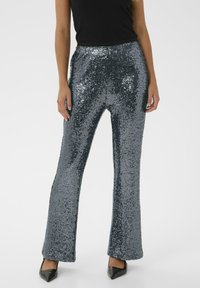 Sprankelende zilveren paillettenbroek met een uitlopende pasvorm, elastische tailleband en een gladde textuur, gecombineerd met zwarte puntige hakken.