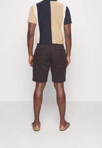 Polo à manches courtes en rayures beige, marine et crème, associé à un short noir. Comprend des poches arrière et une coupe décontractée.