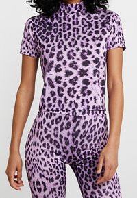 Mujer vistiendo un conjunto de top de manga corta con estampado de leopardo púrpura y leggings de cintura alta frente a un fondo blanco.