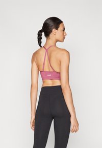 Soutien-gorge de sport rose avec des bretelles croisées, texture lisse et logo dans le dos, associé à un legging noir taille haute.