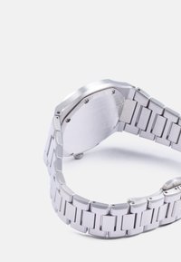 Reloj de pulsera de acero inoxidable con una correa metálica plateada, caja rectangular y un acabado suave y cepillado en la parte posterior y los laterales.