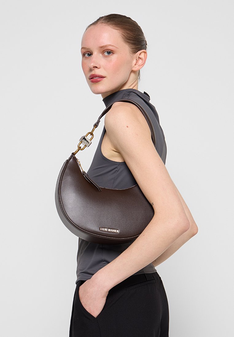 Borsa a mano in pelle marrone con design curvo, dettagli in metallo color oro e tracolla a catena, esposta su uno sfondo neutro.