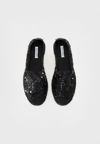 Svarta slips-on skor täckta med paljetter, med rundad tå och texturerad vävd detalj på sulan. Etiketter syns inuti skorna.