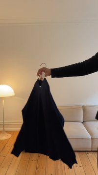 Abito senza maniche blu marino appeso a un gancio, con scollatura a V, tessuto liscio e design fluido, tenuto in una mano contro uno sfondo delicato.