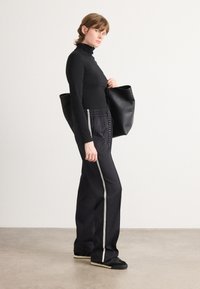 Haut noir à manches longues avec un col montant associé à un pantalon noir ample portant des rayures blanches sur les côtés, et un sac tote noir.