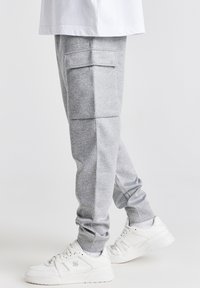 Grå sweatpants med en tapered design, cargo lomme på låret, ribbede manchetter og blød tekstur, parret med hvide sneakers.