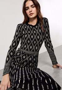 Sukienka dziana z czarno-kremowym geometrycznym wzorem, długimi rękawami, prążkowanymi mankietami, okrągłym dekoltem i dopasowaną talią.