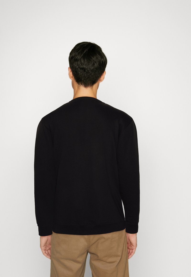 Felpa nera a maniche lunghe con collo a giro, caratterizzata da polsini e orlo a coste. Texture liscia, design minimalista, indossata con pantaloni beige.