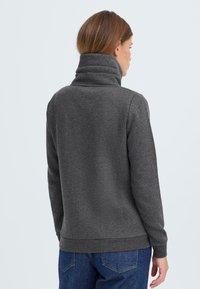 Donkergrijze trui met een hoge kraag, gemaakt van een gestructureerde stof, met een getailleerd ontwerp en lange mouwen, gecombineerd met klassieke blauwe jeans.