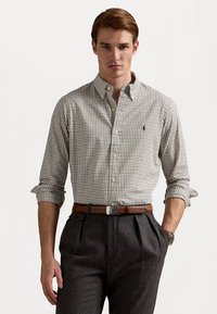 Brun og hvit rutete skjorte med knapp ned-krage, oppbrettede ermer og en liten logo på brystet, kombinert med mørk grå bukser og et brunt belte.