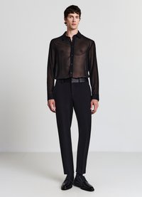 Schwarzes durchsichtiges Hemd mit Knöpfen und maßgeschneiderte schwarze Hose. Das Outfit zeichnet sich durch ein elegantes Design mit glatter Textur und minimalistischen Akzenten aus.