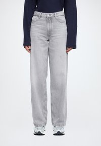 Sivé rifle s vysokým pásom a rovnými nohavicami, vyrobené z džínsoviny. Materiál má jemne opotrebovaný vzhľad. Kombinované s modrými teniskami a dlhým rukávom na vrchu.