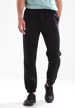 Schwarze Jogginghosen aus Fleece mit elastischem Bund und Kordelzug, Bündchen an den Knöcheln und Seitentaschen, kombiniert mit schwarzen Sportschuhen.