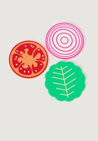 Tres posavasos de silicona coloridos con forma de rodaja de tomate, rodaja de cebolla y hoja verde sobre un fondo claro.
