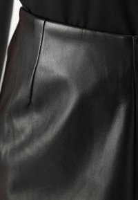 Zwarte leren rok met een gladde textuur, voorzien van een platte taille en subtiele kreuken. Slanke en figuurvolgende uitstraling.