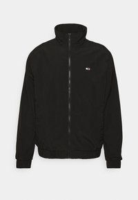 Black zip-up jacket with high collar, elastic cuffs, and hem. Features a small color logo on the chest, made from lightweight fabric.