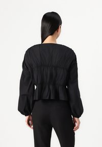 Fekete, hosszú ujjú blúz összegyűrt derékkal és puffos ujjal. Sima anyag, formázott szabással és finom textúrájú részletekkel a háton.