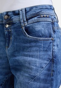 Blauwe denim jeans met een middelhoge taille, een ritsluiting, decoratieve metalen accenten en subtiele vervaging in de stof.