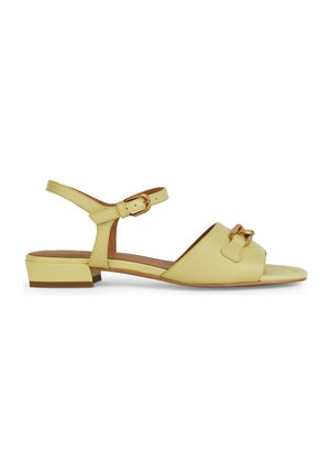Sándalo de cuero amarillo con un tacón bajo, punta abierta, correa de tobillo ajustable y una hebilla decorativa en la parte frontal.