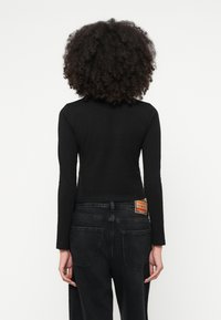 Čierny crop top s dlhým rukávom v kombinácii s čiernymi džínami s vysokým pásom. Džínsy majú vzadu béžovú nášivku s textom a dve zadné vrecká.